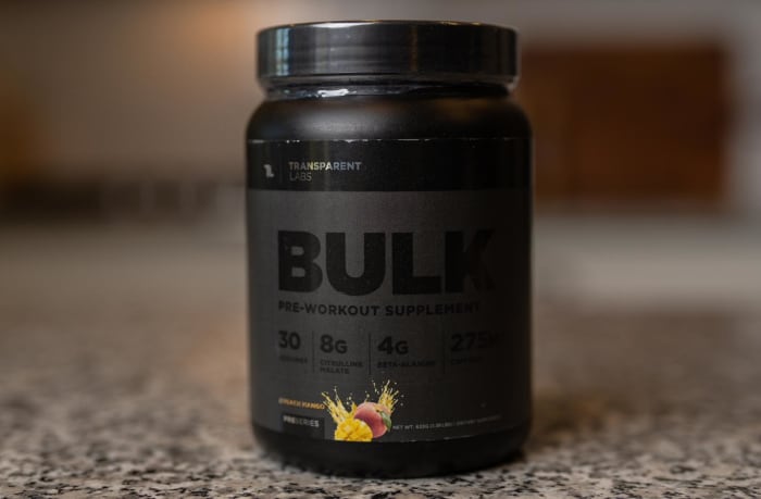 A black tub of Transparent Labs Bulk Black pre-workout supplement in Peach Mango flavor on a granite countertop